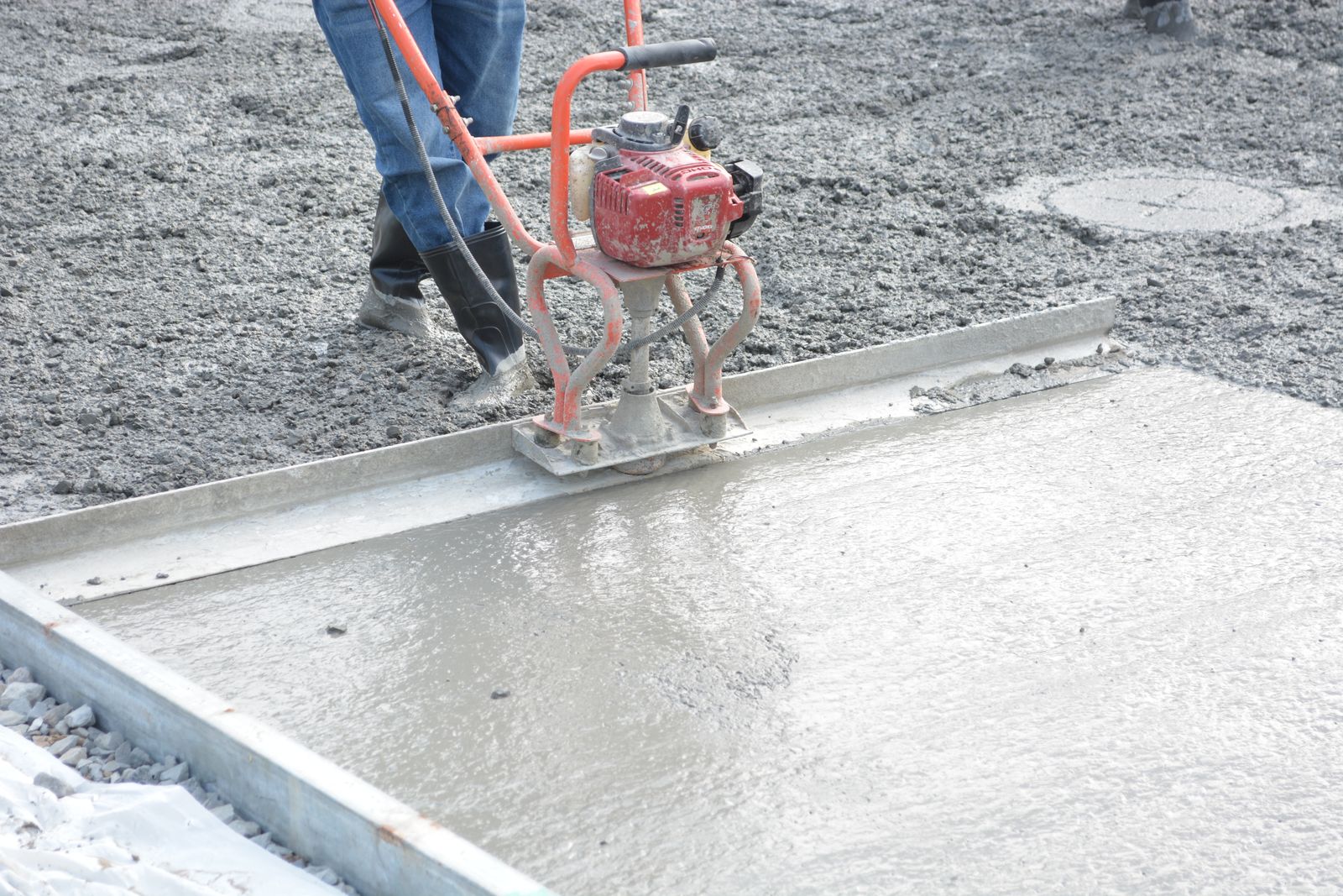 A worker running a power screed across a fresh concrete slab held in steel forms