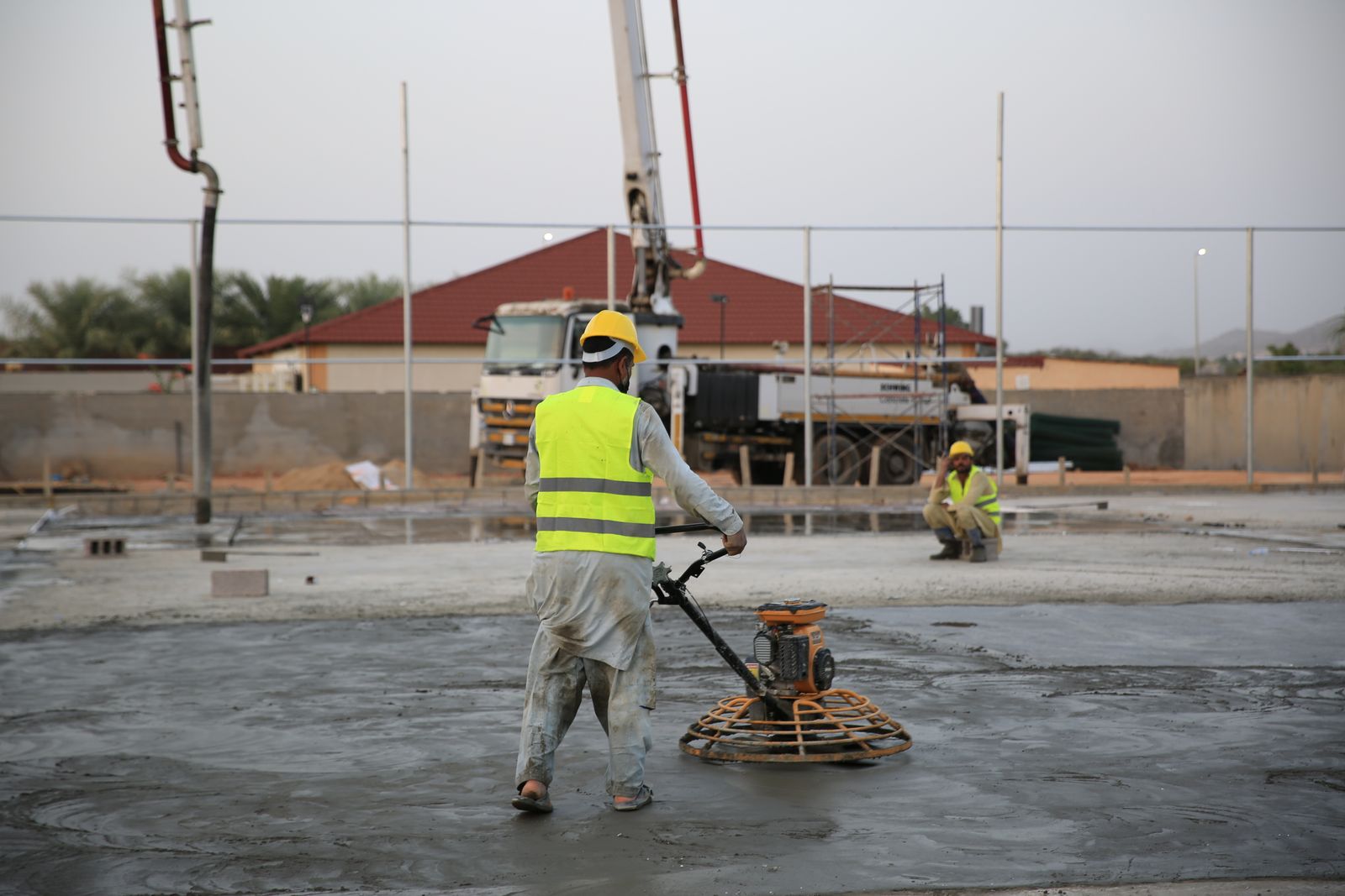 A finisher running a power trowel across a large fresh concrete slab to bring up a smooth surface